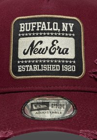Gorra color burdeos con un parche en blanco y negro que dice "Buffalo, NY", "New Era" y "Establecido en 1920". Con correa ajustable en la parte trasera.