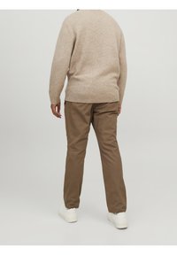 Maglione beige lavorato a maglia con scollo rotondo, abbinato a pantaloni marroni a gamba dritta e sneakers bianche. Texture liscia su tutta la superficie.