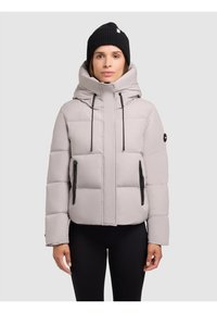 Lys grå pufferjakke med høj krave, lynlåslommer i sort og en snørret hætte. Ribbet sort beanie båret på hovedet.