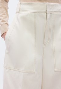 Μπεζ παντελόνι με φαρδιά μπατζάκια και ψηλή μέση, με μεγάλες μπροστινές τσέπες και αντίθετες ραφές, προσφέροντας απαλή και λεία υφή.