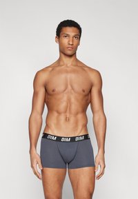 Graue Boxer-Slips mit einem schwarzen Bund, der das "DIM"-Logo in Weiß trägt. Sie bestehen aus glattem Stoff, haben eine enganliegende Passform und eine Länge bis zur Mitte des Oberschenkels.