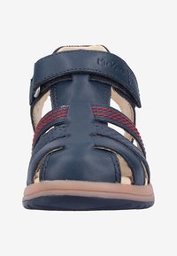 Blå lädersandal med röda detaljer, öppen design, justerbara remmar och gummisulor. Har flera urtag för ventilation.