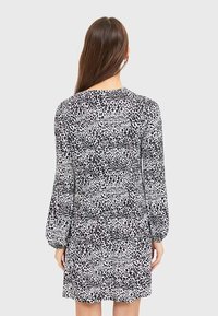 Robe à imprimé léopard noir et blanc avec de longues manches bouffantes et un col rond, présentant une coupe décontractée et une texture de tissu douce.
