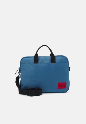 Serviette rectangulaire bleue avec poignées noires, une bandoulière réglable et un écusson rouge du logo Hugo en bas à droite sur le devant.