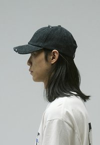 Black denim baseball cap with a slightly curved brim, distressed design, and logo on the front. Worn with a light-colored shirt.