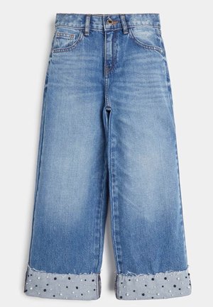 Niebieskie dżinsy z szerokimi nogawkami i postrzępionym brzegiem, z kontrastującym mankietem w czarno-białe kropki. Standardowy krój z pięcioma kieszeniami.