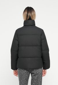 Svart puffjakke med høy krage, med quiltede seksjoner og en glatt overflate. Brukt med leopardmønstret bukser.