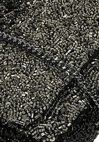 Kovové hardwarové prvky a články řetězu proplétající se s tmavým, texturovaným pozadím různých kovových prvků v stříbrných a černých tónech.