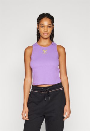 Top corto morado de material acanalado, con un logo amarillo bordado en el pecho. Combinado con pantalones de chándal negros.