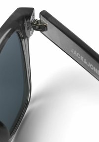 Occhiali da sole neri con lenti grigie, che mostrano una montatura in plastica lucida e una cerniera metallica. Marchio "JACK & JONES" sulla stecca.