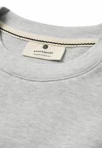 Grauer Sweatshirt mit geripptem Kragen, strukturiertem Inneren und einem cremefarbenen Etikett mit schwarzem Text. Die Nähte entlang des Kragens sind ebenfalls schwarz.