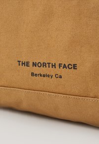 Brown fabric bag featuring "THE NORTH FACE" and "Berkeley Ca" printed in black. Simple design with a textured surface and visible stitching.