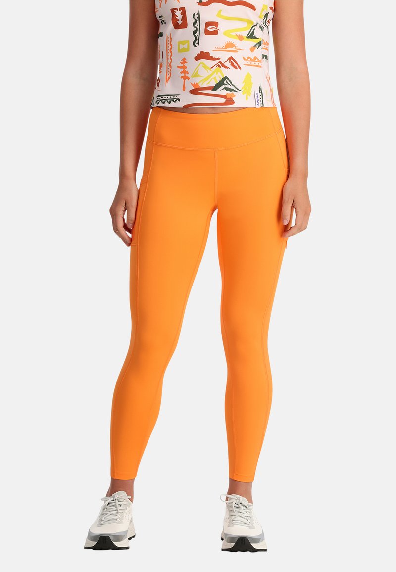 Leggings arancioni con una texture liscia e elastica, design aderente e vita alta. Abbinati a un top con motivo e scarpe da ginnastica bianche.