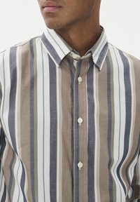 Moški oblečen v srajco s dolgimi rokavi na gumbe z navpičnimi črtami v modri, bež, beli in olivno zeleni barvi.