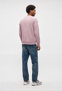 Gaiši rozā sudraba arapa krekls ar apaļu kakla izgriezumu, valkāts virs zila džinsa. Balti un pelēkiSporta apavi piešķir kontrastu apģērbam.