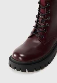 Botas de cuero burdeos con cordones, puntera redonda, ojales de metal y una suela de goma negra gruesa con un diseño de relieve.