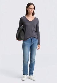 Mørkegrå v-hals langærmet top, lyseblå jeans og hvide sneakers. Model med en sort håndtaske. Glat tekstur og tætsiddende design.