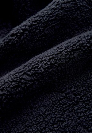 Tumšs jūras zils, biezs audums ar mīkstu, teksturētu virsmu, kas rotāta ar vilnainu rakstu. Materiāls izskatās biezs un ērts.