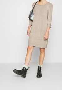 Beige stickad klänning med trekvartslånga ärmar, kombinerad med svarta läderankelstövlar och mintgröna volangstrumpor. Väska med svart och vitt mönster.