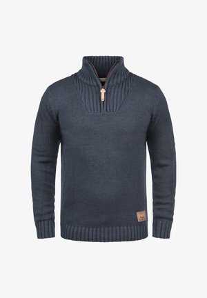 Pletený námorní svetr s vysokým límcem, s polo-zip uzavřením, žebrovanými manžetami a texturovaným vzorem na horní části. Kožená ozdobná etiketa.