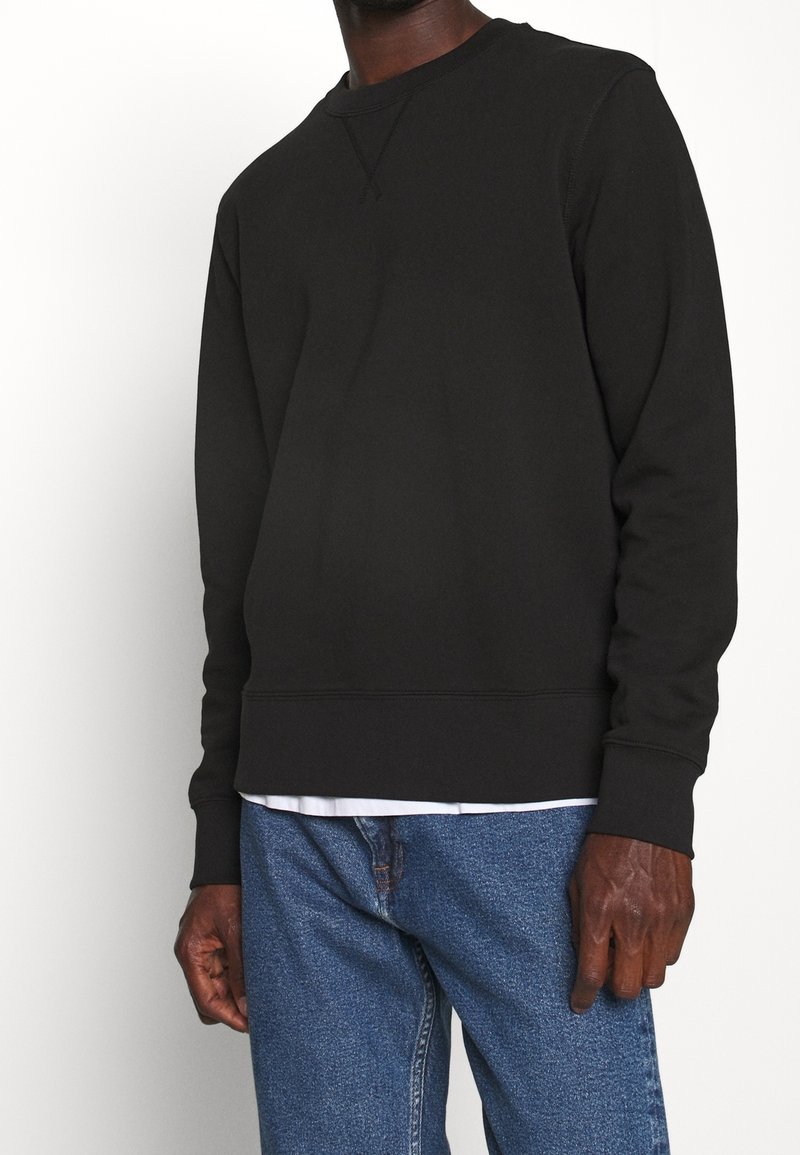 Schwarzer Pullover mit Rundhalsausschnitt, gerippten Bündchen und Saum, kombiniert mit blauen Jeans mit einer glatten, weichen Textur.