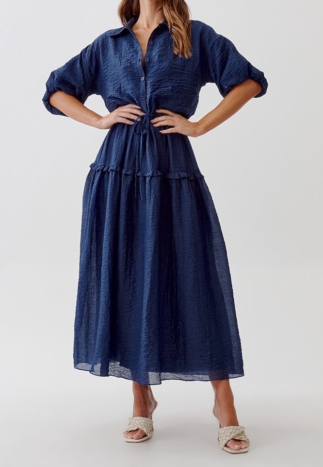 Marinblå lång klänning i krinklad tyg, med knappstängning fram, korta ärmar och en flerlagerskjol med volangdetaljer.