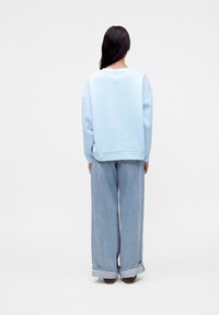 Personne aux longs cheveux foncés vue de dos portant un sweat-shirt bleu clair et un jean bleu clair à jambes larges avec des revers.