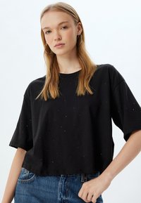 Czarny bawełniany krótki t-shirt z luźnym krojem, krótkimi rękawami i rozsianymi ozdobami. Połączony z niebieskimi dżinsami.