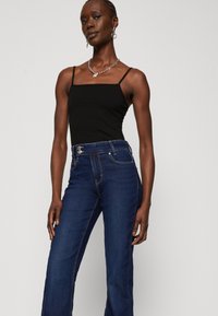 Schwarzes Spaghetti-Trägershirt kombiniert mit hochtaillierten dunkelblauen Jeans mit Knopfverschluss und Fronttaschen. Strukturierter Denimstoff.