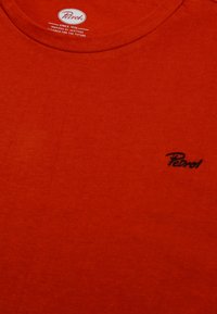 Červené bavlněné tričko s kulatým výstřihem a malým, černým logem "Petrol" vyšitým na prsou. Hladká textura, jednoduchý design.