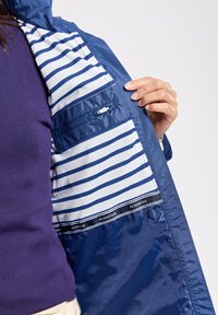Giubbotto navy con fodera a righe blu e bianche. Presenta una tasca con zip sulla fodera. Tessuto morbido e design leggero.