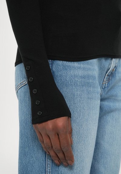 Top negru cu mânecă lungă, cu un design ajustat, având detalii cu nasturi pe manșetă, asortat cu blugi decolorati bleumarin.