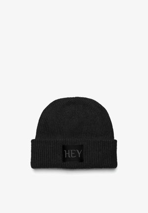 Zwarte gebreide beanie met een geribbelde textuur en een omgeslagen rand. Bevat een zwart rechthoekig label met het woord "HEY" in grijze letters.