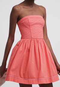 Korálové šaty bez ramínek s texturovaným, vyšívaným živůtkem a širokou, nabranou sukní. Mají rovný výstřih a jemné šití ve spodním lemu.