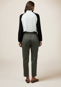 Maglia a maniche lunghe grigia chiara e nera con colletto alto, abbinata a pantaloni a quadri verdi con vita elastica e gambe affusolate.