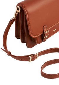 Smeđa kožna torba preko tijela s zlatnim kopčama, podesivim remenom, dvostrukim odjeljcima i bijelim detaljima šivanja.