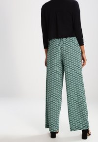 Pantalon à jambes larges vert avec un motif géométrique noir, en tissu léger. Doté d'une taille élastique et d'une coupe fluide.