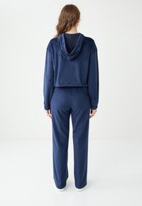 Marineblauw velours trainingspak bestaande uit een cropped hoodie met capuchon en lange mouwen, gecombineerd met loszittende broek, met een zachte textuur.