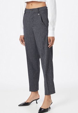 Nainen, joka käyttää korkevavyötäröisiä harmaita räätälöityjä housuja, joissa on etutaitokset, yhdistettynä valkoiseen pitkähihainen lyhyt puseroon ja mustiin matalakorkoisiin kenkiin.