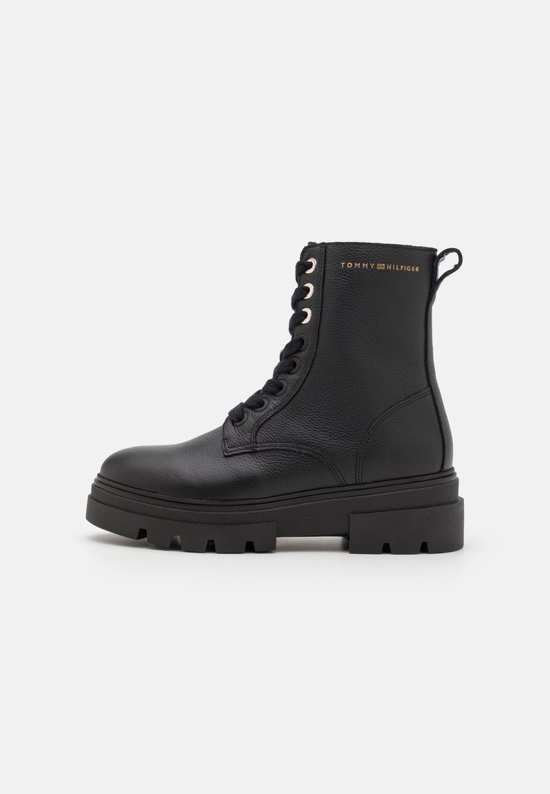 Botte de combat noire en cuir à lacets avec semelle épaisse à crampons et languette, avec le logo doré "Tommy Hilfiger" sur le côté.