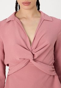 Rotes Kleid mit geknoteter Vorderseite und V-Ausschnitt, langen Ärmeln und strukturiertem Stoff. Subtile Glanz und entspannte Silhouette.