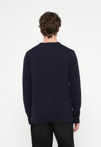 Maglione a collo rotondo in maglia blu navy, con polsini e orlo a costine e design a spalla senza cuciture. Vista posteriore mostrata.