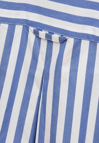 Blue and white striped fabric featuring a texture with a flat, woven appearance. Notable details include a small loop and stitching.