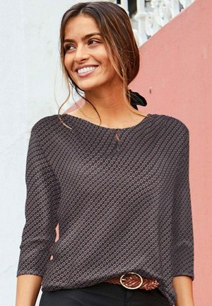 Black patterned blouse with three-quarter sleeves, featuring a subtle geometric design and a rounded neckline; paired with a woven brown belt.