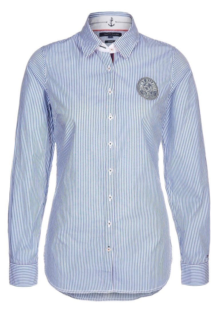 Camisa de manga larga a rayas en azul claro y blanco con cierre de botones en la parte delantera, cuello puntiagudo y parche redondo con el logo en el pecho izquierdo.