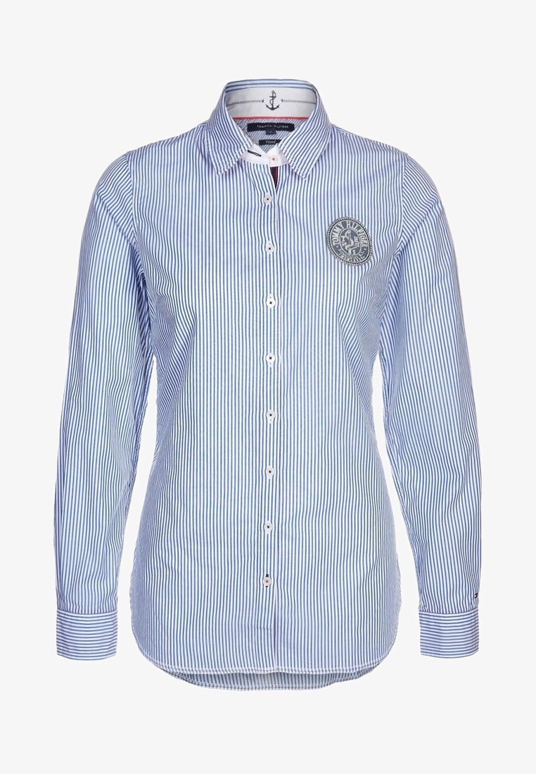 Camisa de manga larga a rayas en azul claro y blanco con cierre de botones en la parte delantera, cuello puntiagudo y parche redondo con el logo en el pecho izquierdo.