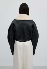Zwarte leren jas met een luxe crèmekleurige kraag, oversized stijl en textuurovervlak. Gecombineerd met beige high-waisted broeken.