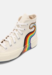 Baskets montantes blanches en toile avec lacets blancs présentant un motif de vague arc-en-ciel coloré sur le côté et la semelle.
