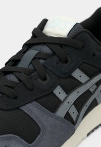 Gros plan d'une basket de sport noire et grise avec des lacets noirs et des bandes de marque gris clair sur le côté.