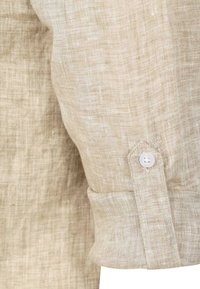 Lichtbeige linnen shirt met een gestructureerde afwerking, voorzien van een knoopmanchet en subtiele geweven patronen. Close-up van de mouwdetail.